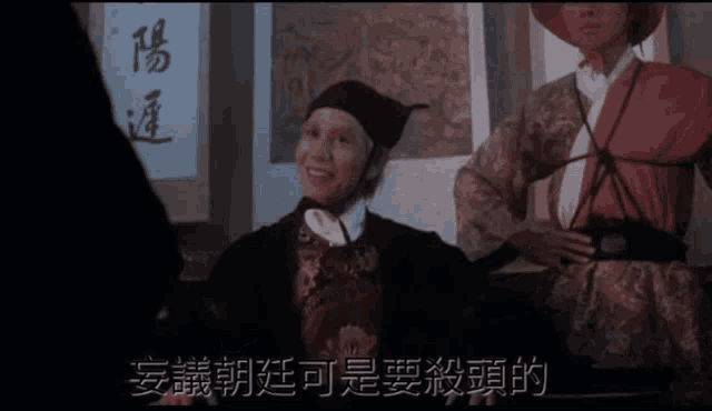 a man in a hat is talking to another man with chinese writing on the wall behind them