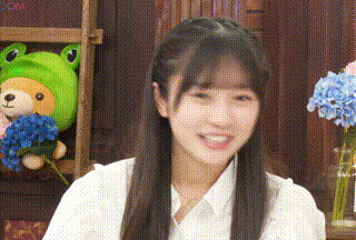a young girl is smiling in front of a frog stuffed animal and flowers .