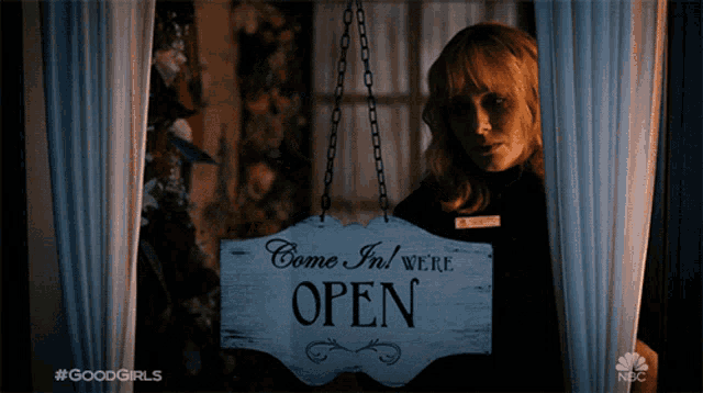 a woman holding a sign that says " come in we 're open "