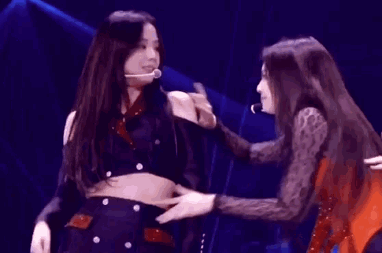 two women are standing next to each other on a stage and one is touching the other 's hand .