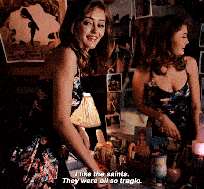 a woman in a floral dress says " i like the saints they were all so tragic " in front of a mirror