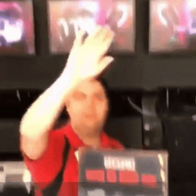 a man in a red shirt is making a funny face while sitting at a desk in front of a computer .