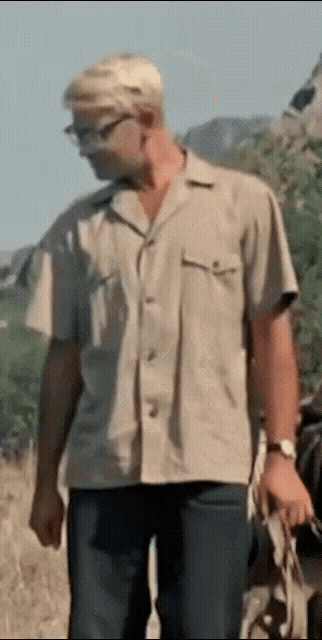 a man wearing glasses and a tan shirt is walking down a road .