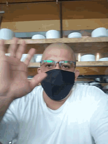 a bald man wearing glasses and a black mask waves his hand