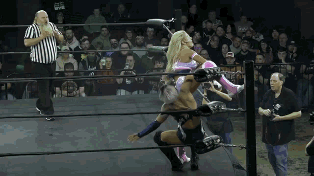 a wrestler in a pink outfit is being lifted in the air by another wrestler while a referee watches