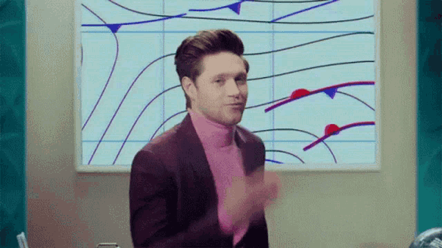 a man in a suit and pink turtleneck is standing in front of a painting on a wall .