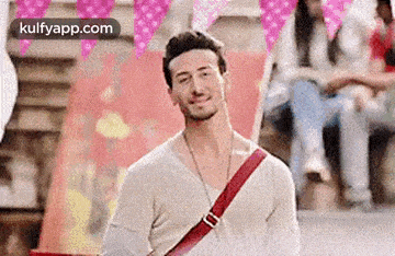 a man wearing a white shirt and a red sling bag is smiling and looking at the camera .