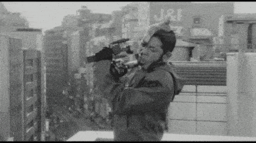 a black and white photo of a man holding a camera in front of a building with j & f written on it