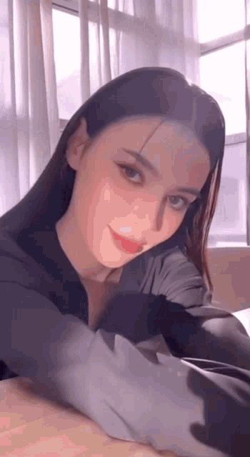 a woman is sitting at a table in front of a window and smiling .