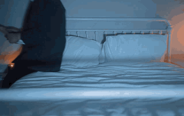 a man in a suit sits on a bed with white sheets and pillows