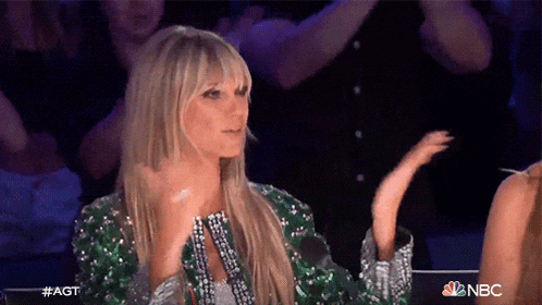 a woman in a green sequined jacket is clapping her hands while sitting in front of a crowd .
