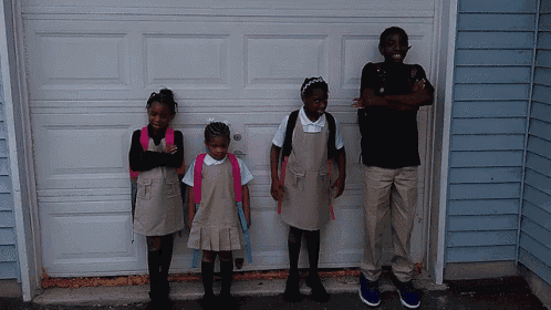 four children in school uniforms standing in front of a garage door