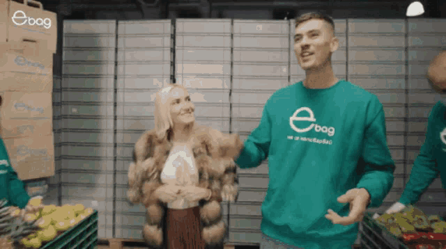 a man wearing a green ebag sweatshirt stands next to a woman in a fur coat