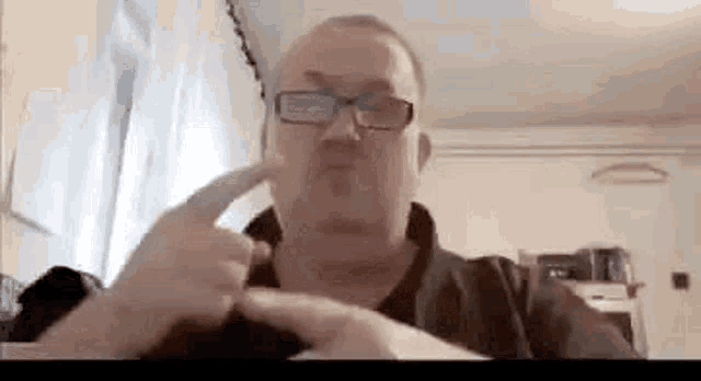 a man wearing glasses is blowing a kiss at the camera while sitting in a living room .
