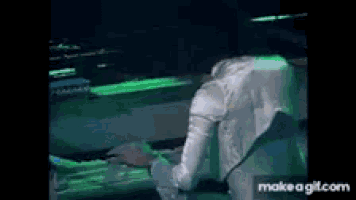 a man is playing a keyboard in a dark room with green lights behind him .