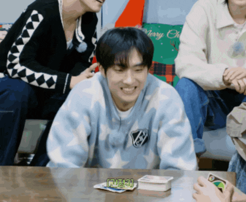 a man wearing a sweater that says merry christmas sits at a table with cards on it