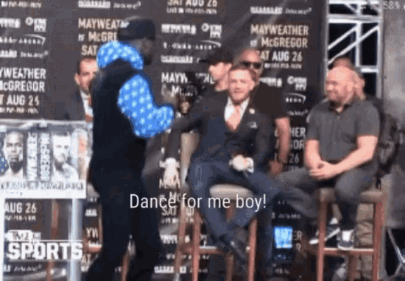 a man in a blue jacket says dance for me boy in front of a group of men