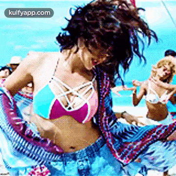 a woman in a bikini is dancing on a beach with other people .