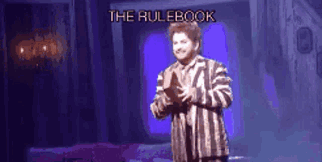 a man in a striped shirt is standing on a stage with the rulebook written on it