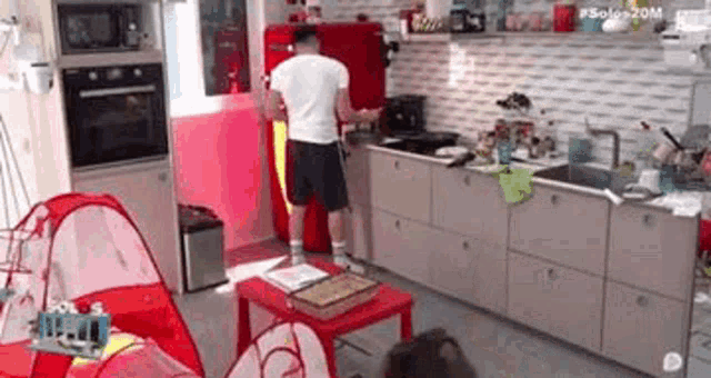 a man is standing in a kitchen with a red refrigerator and a red table .