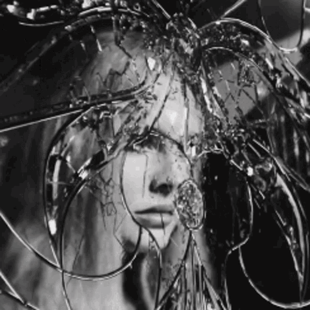 a black and white photo of a woman behind a broken mirror