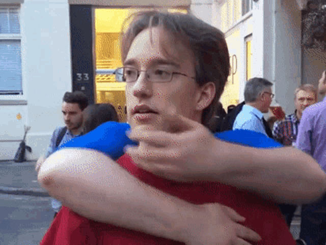 a man wearing glasses and a red shirt is being hugged by a woman in front of a building with the number 33 on it