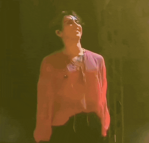 a man in a pink shirt is dancing on a stage in the dark .