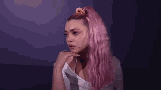 a woman with pink hair and a flower in her hair looks sad