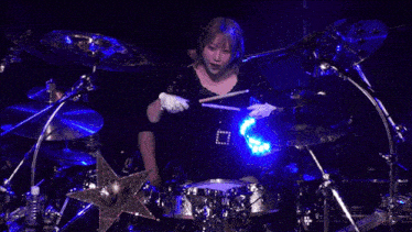 a woman is playing a drum set with a blue light behind her