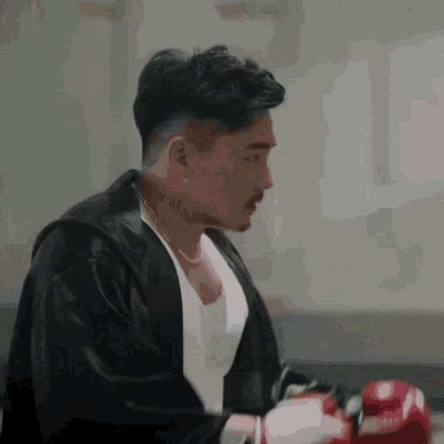 a man wearing boxing gloves and a black jacket looks to his left