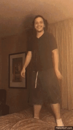 a man in a black shirt and green shorts is dancing on a bed