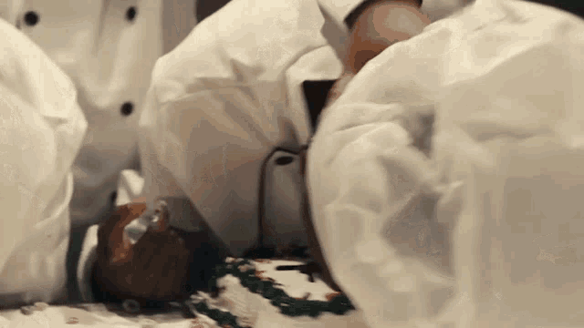 a man in a chef 's hat is laying on a table with a cake on it .