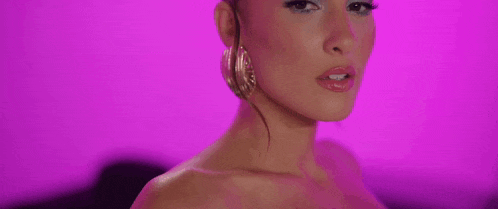 a close up of a woman 's face with a purple background . she is wearing hoop earrings .
