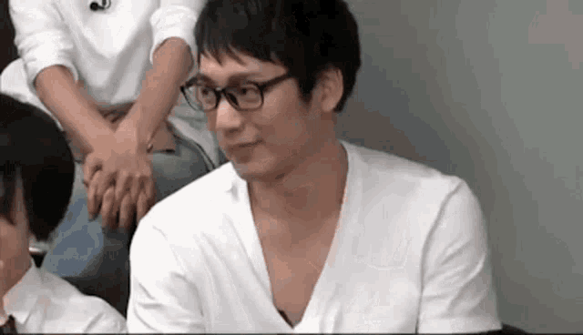 a man wearing glasses and a white shirt is sitting at a table with other people .