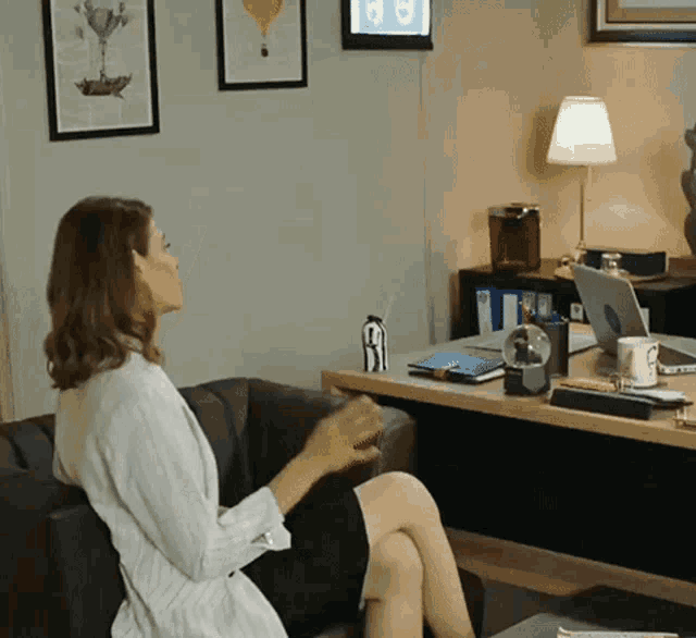a woman sits on a couch with her legs crossed in front of a desk with a laptop