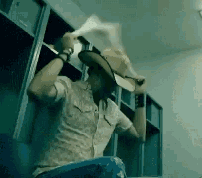 a man wearing a cowboy hat is sitting in a locker room holding a paper .