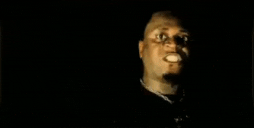 a man with a necklace around his neck is looking at the camera in the dark .