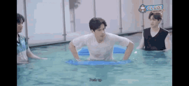 a group of young men are swimming in a pool . one of the men is wearing a white shirt .