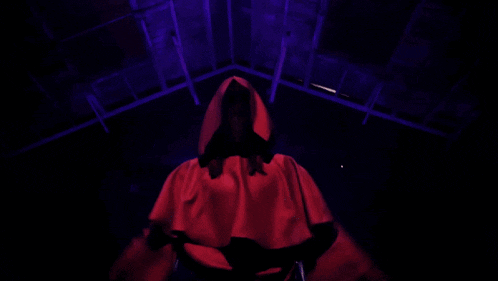 a person in a red robe with a hood is standing in a dark room with their arms outstretched