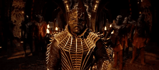 a man in a gold costume is standing in front of a crowd of people in a dark room .