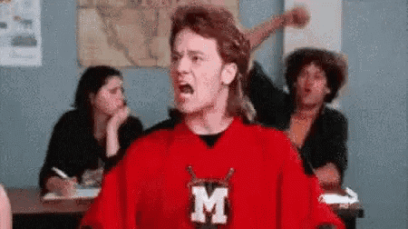 a man wearing a red jersey with the letter m on it is sitting in a classroom .