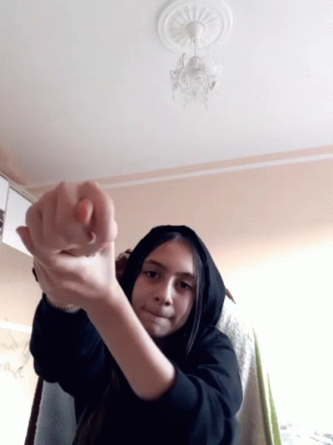 a girl wearing a black hoodie is making a heart shape with her hands