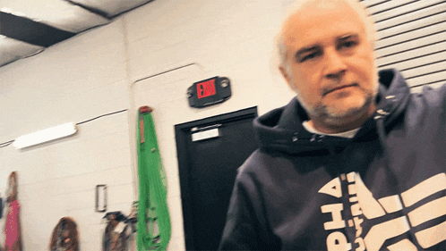 a man in a blue hoodie stands in front of a red exit sign