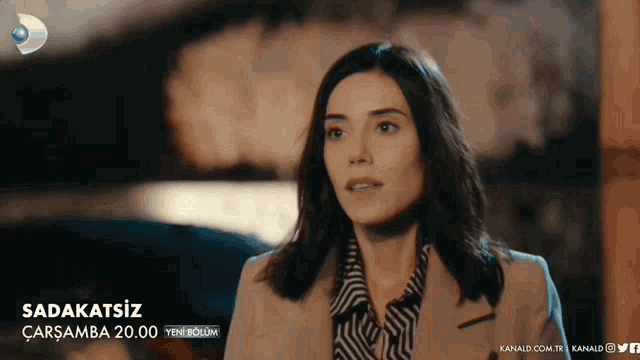 a woman in a striped shirt and a tan jacket is featured in a video for sadakatsiz