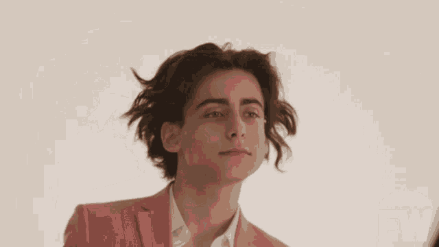 a young man in a pink suit is smiling in front of an ew advertisement