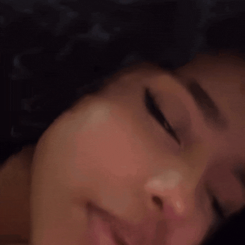 a close up of a woman 's face with her eyes closed and her hand in her mouth