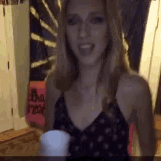 a woman in a black tank top is smiling and holding a cup