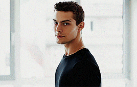 a young man in a black shirt is standing in front of a window looking at the camera .