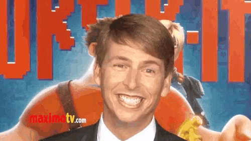 a man in a suit and tie is smiling in front of a maximtv.com ad