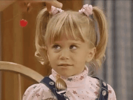 a little girl is sitting in a chair with a spoon in her mouth and a cherry in her hair .